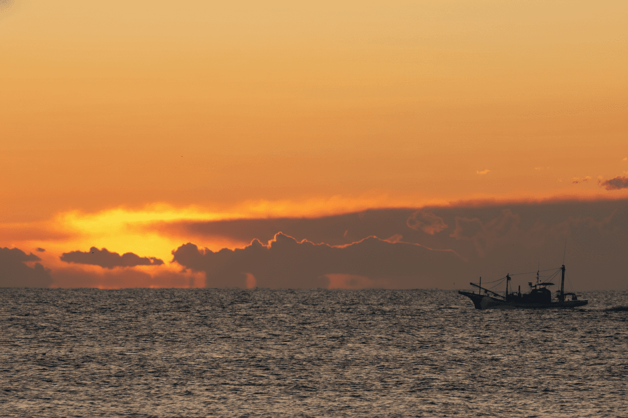 Fishing boat silhouetted against blazing ocean sunset — sustainable maritime commerce
