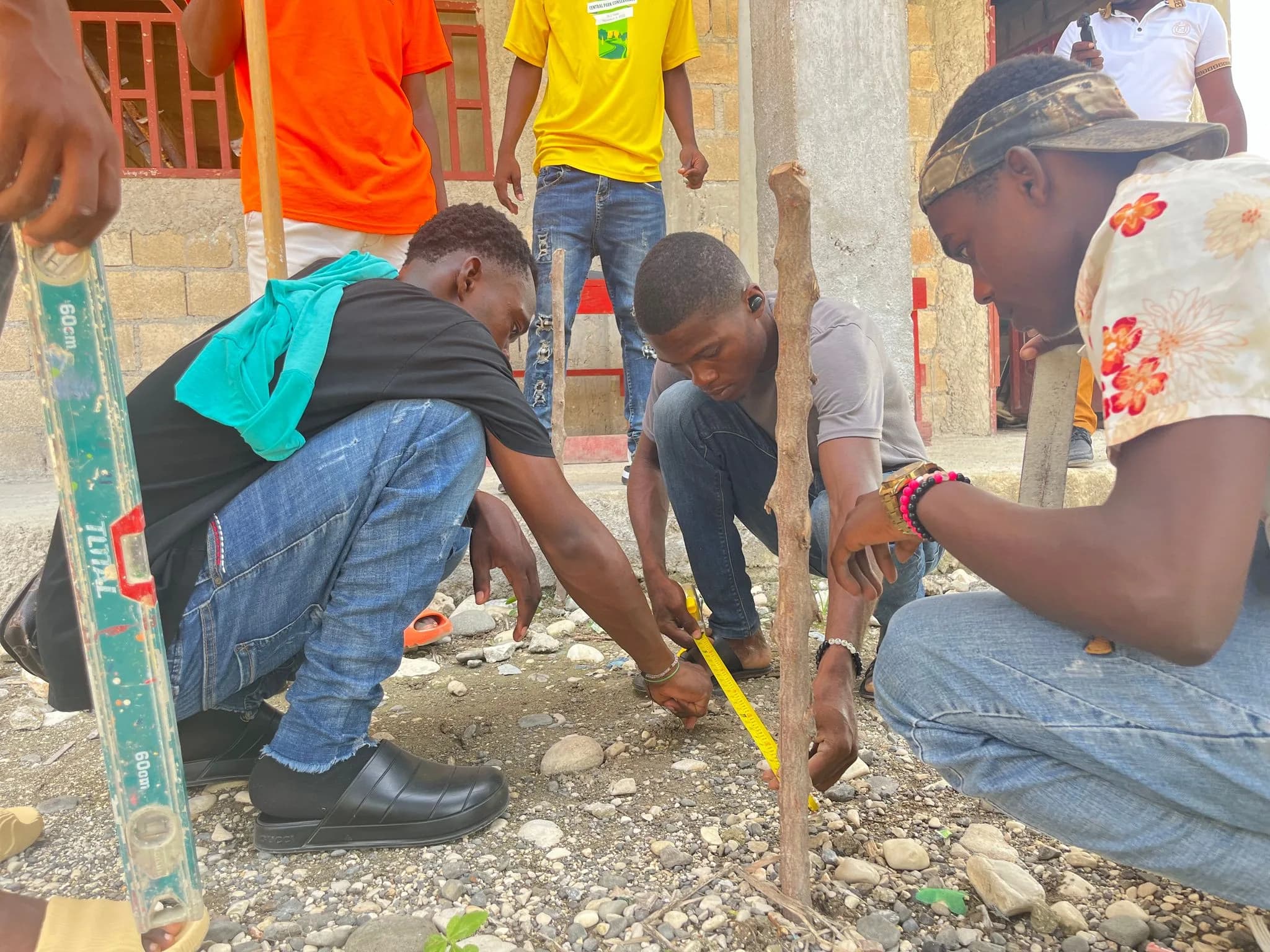 Students kneeling with a tape measure and a wooden stake on a gravel site
