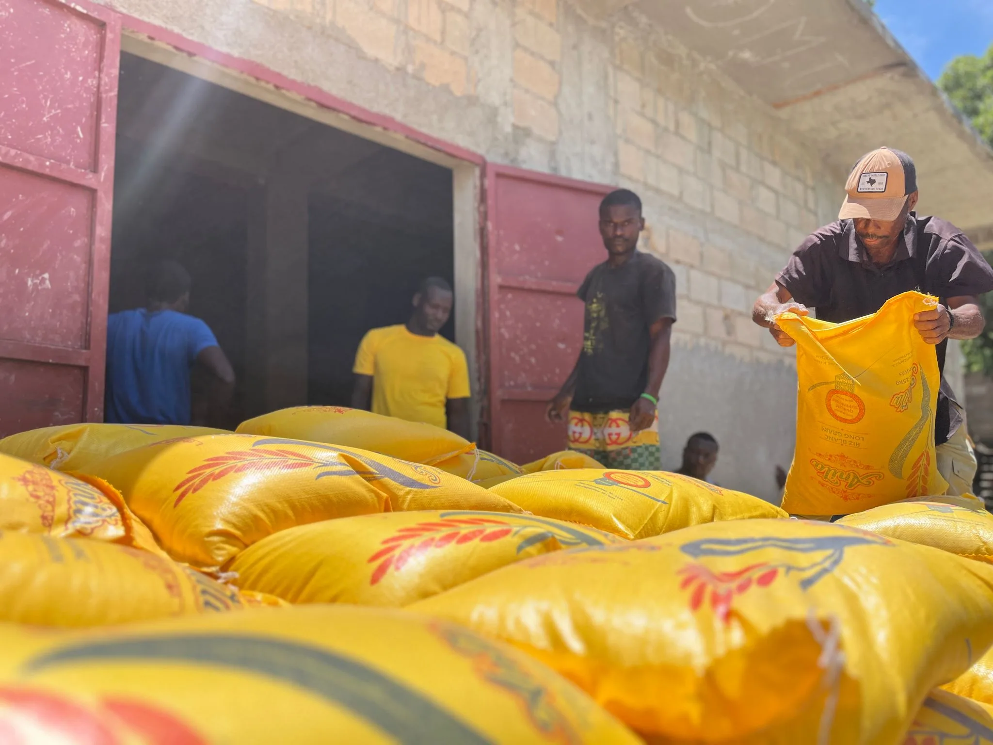 Yellow sacks of rice stacked in a doorway while staff unload more