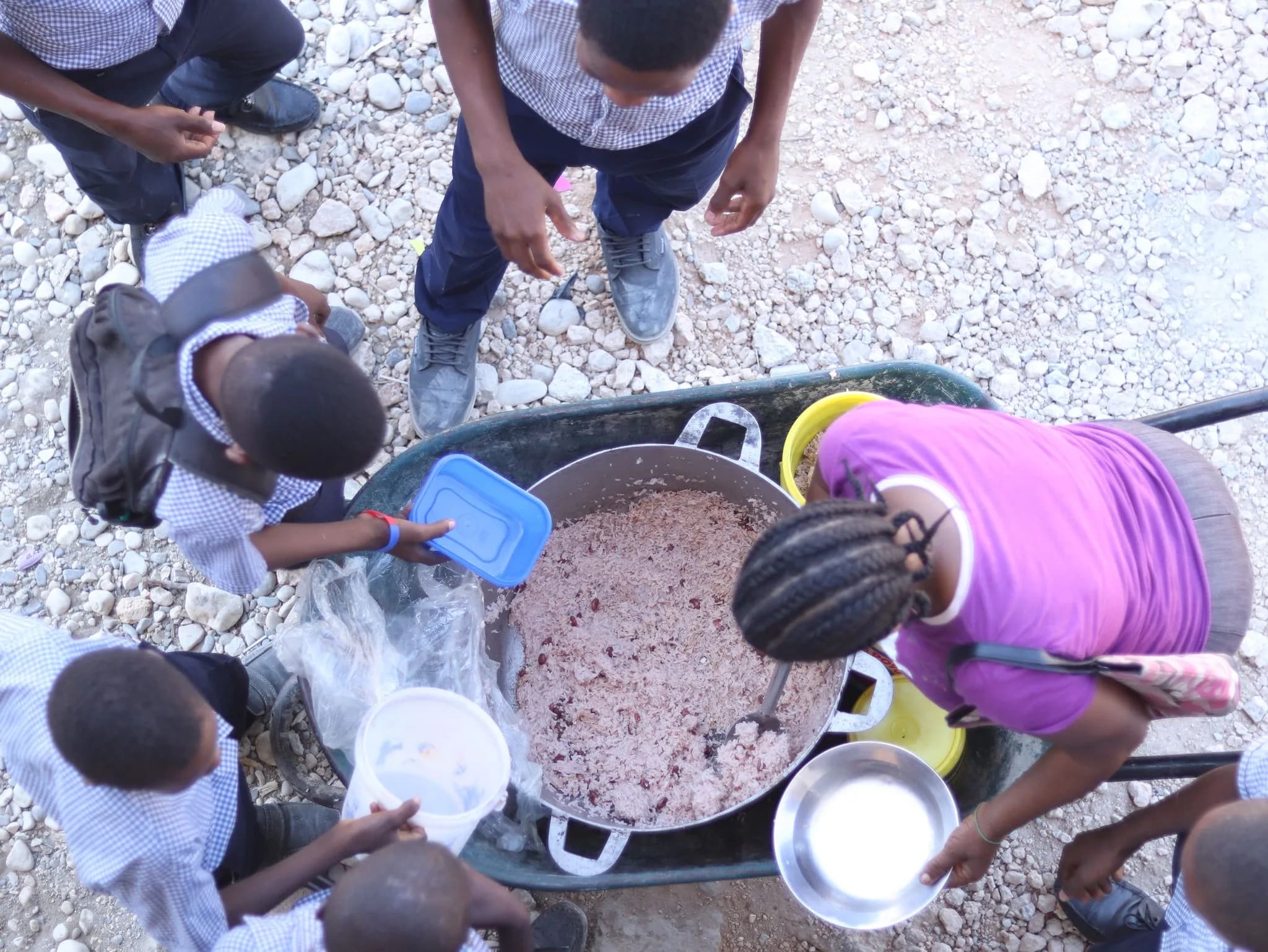 Looking down on a large pot of rice and beans in a wheelbarrow, with students holding containers