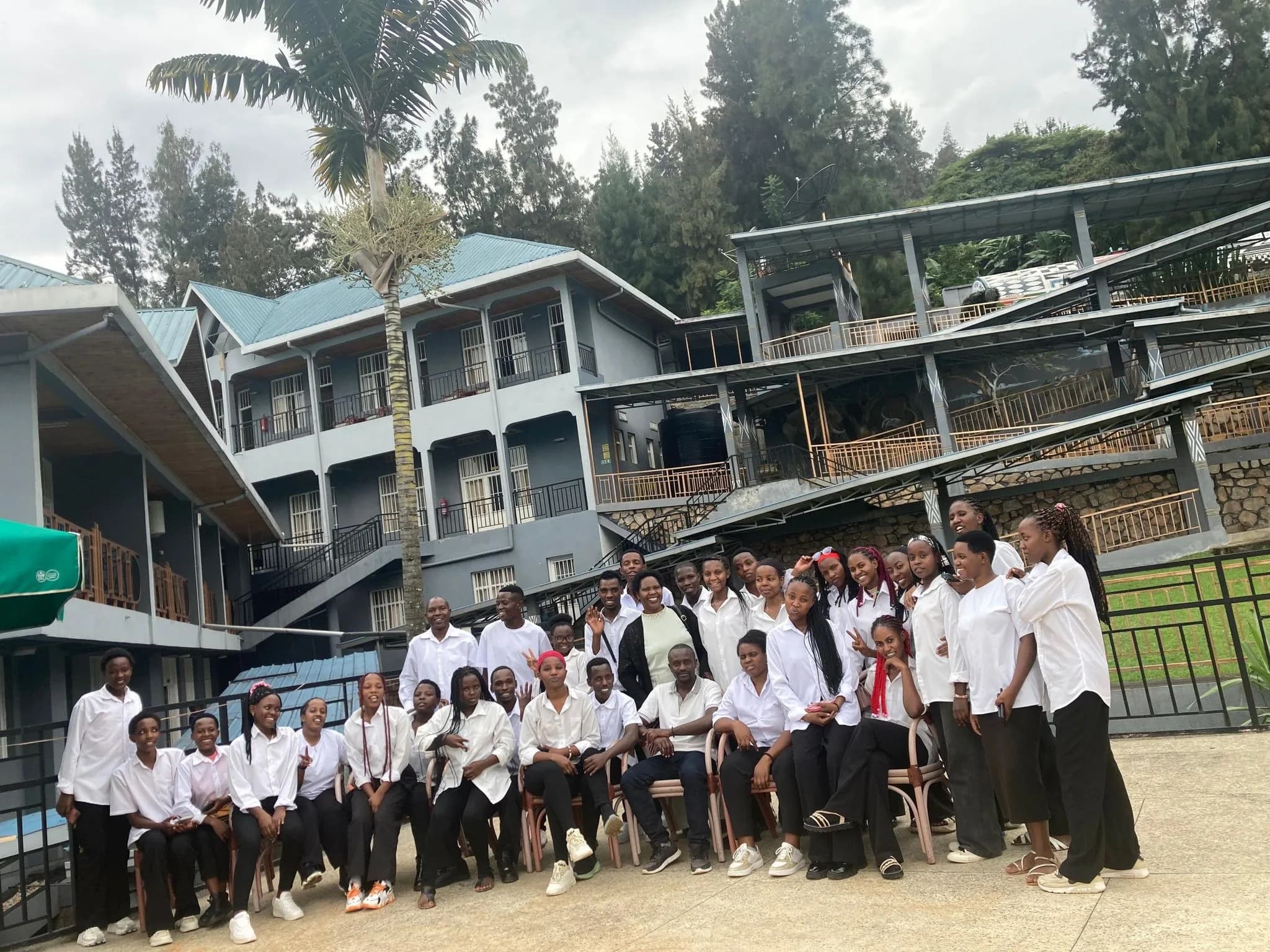 A large group of students in white shirts posing in front of a multi-storey hotel