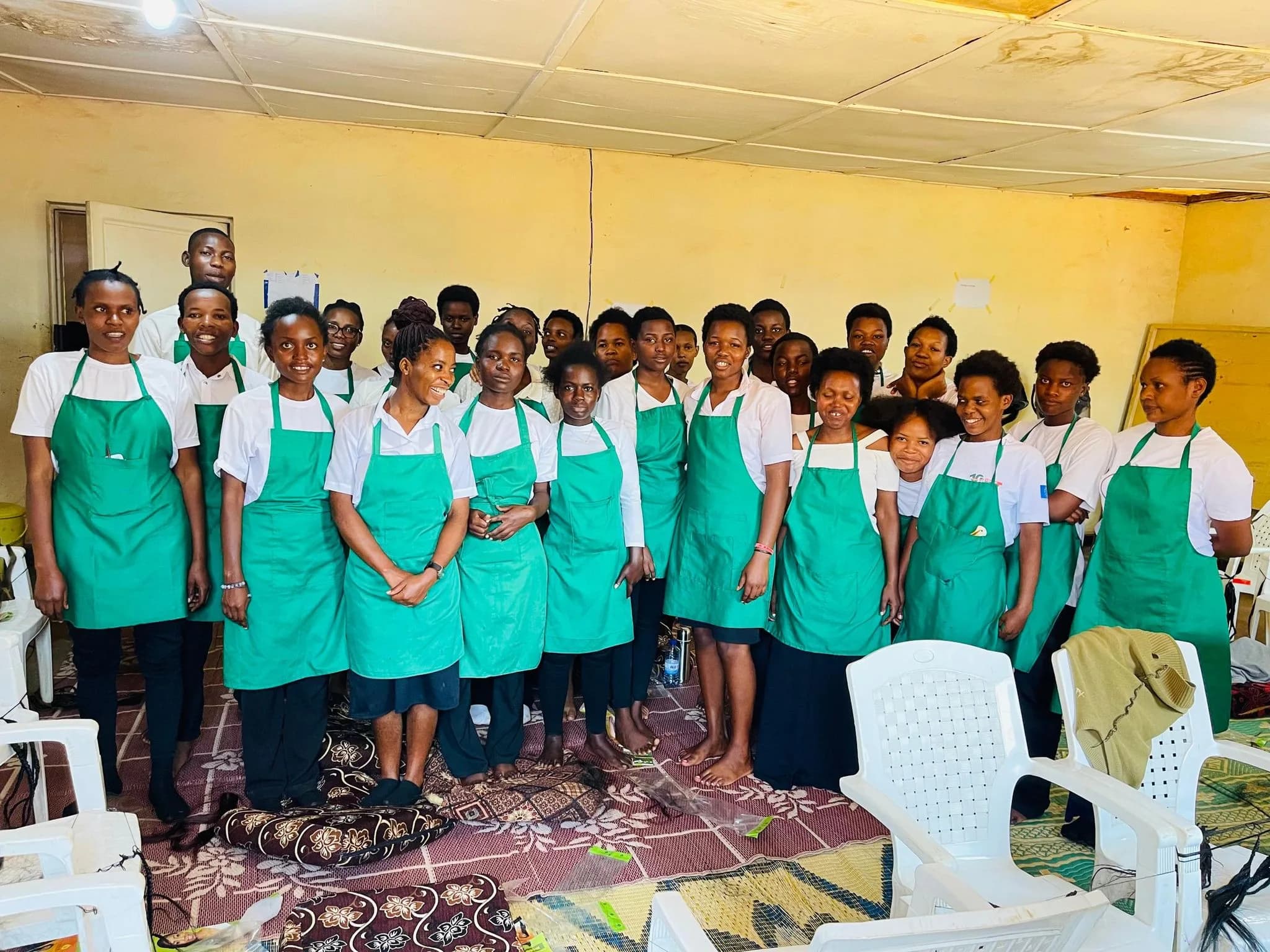 About forty hairdressing students in green aprons standing together in a classroom