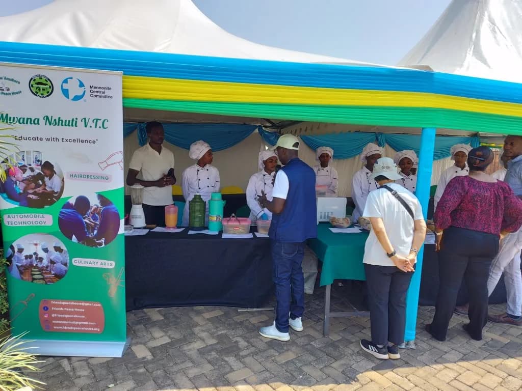 Students in chef whites at an exhibition stall under a tent with a school banner
